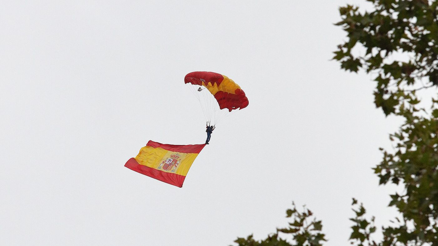 Un paracaidista de la PAPEA desciende con una gran bandera de España colgando bajo él