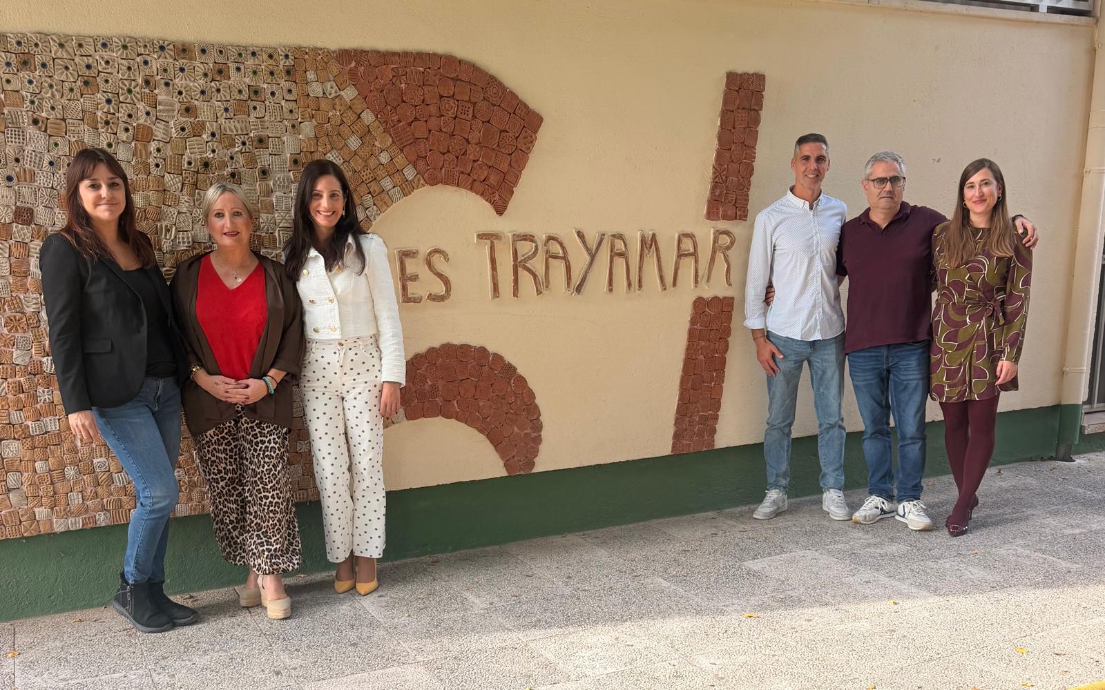 Seis personas adultas posan de pie junto a una pared con un mural de azulejos y el texto ES TRAYAMAR.