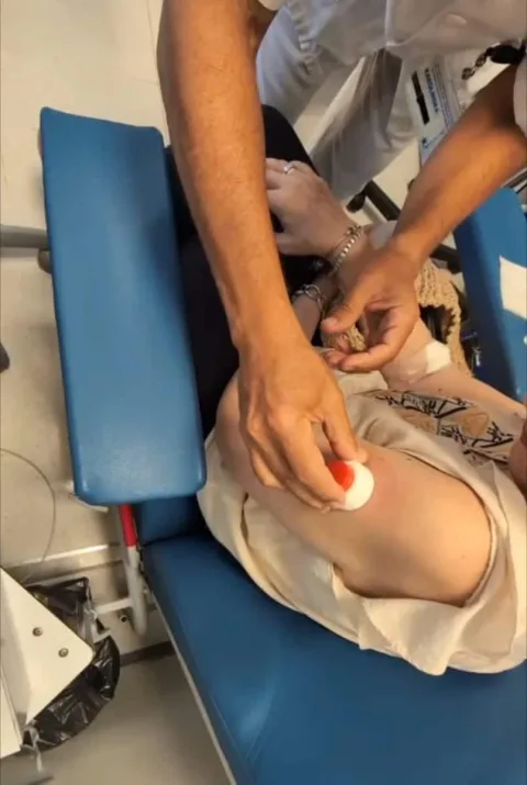 Una persona sentada en una camilla azul recibe un pinchazo en el brazo con un algodón con sangre.