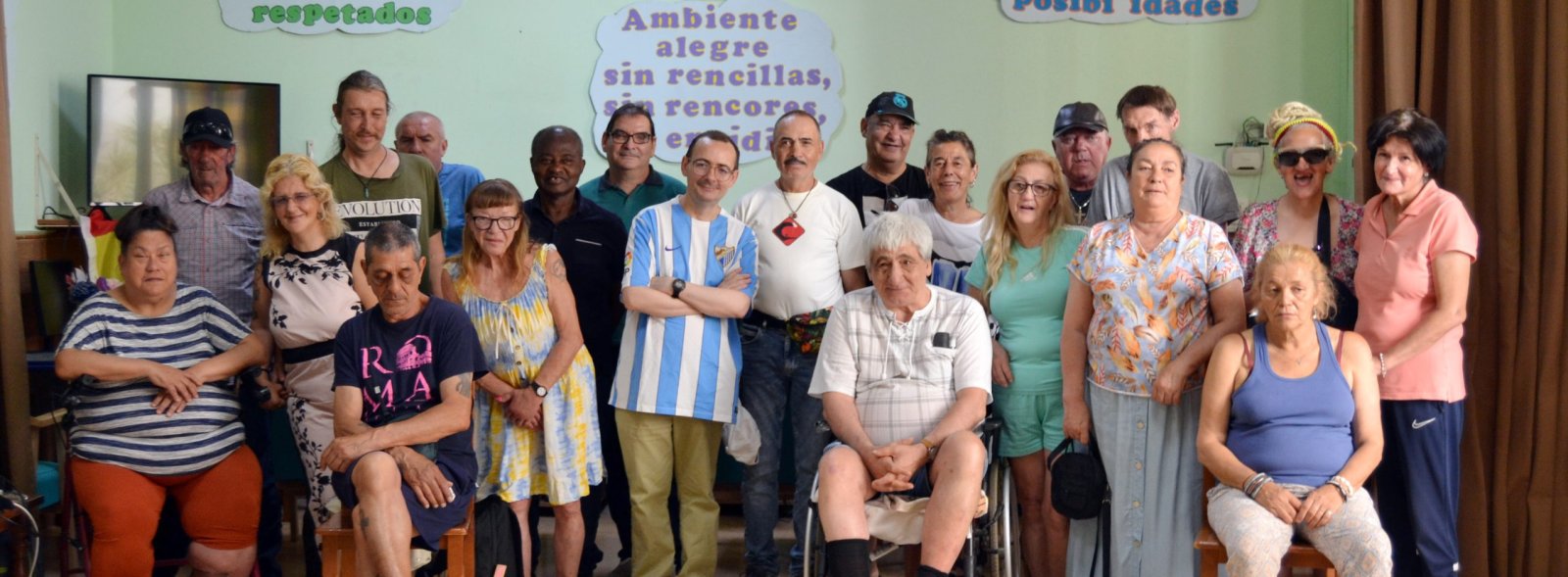 Un grupo de unas veinte personas posa de pie y sentadas en una sala con carteles en la pared que dicen respetados, Ambiente alegre sin rencores y Posibilidades.
