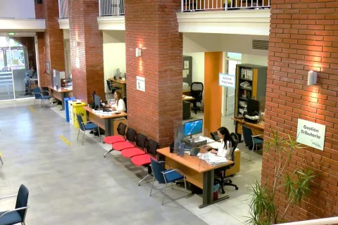 Interior de una oficina con columnas de ladrillo, mostradores, sillas rojas y un cartel de Gestión Tributaria.