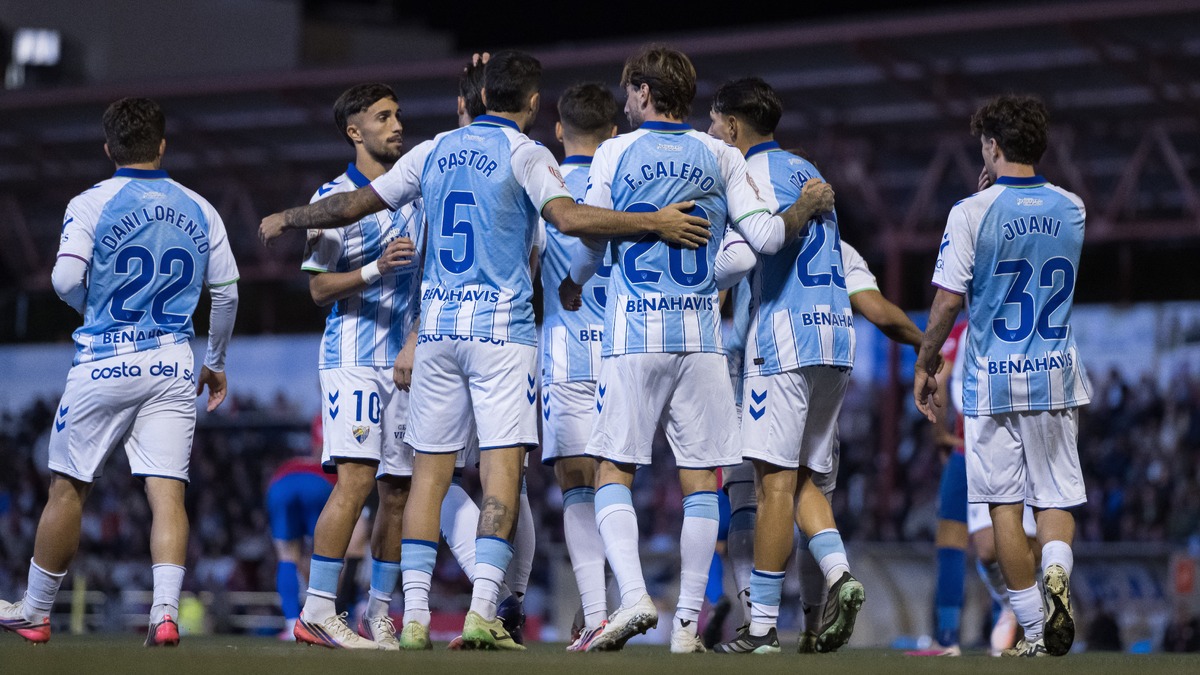 Varios jugadores de fútbol con camiseta azul y blanca de rayas se abrazan en grupo sobre el césped de un estadio.