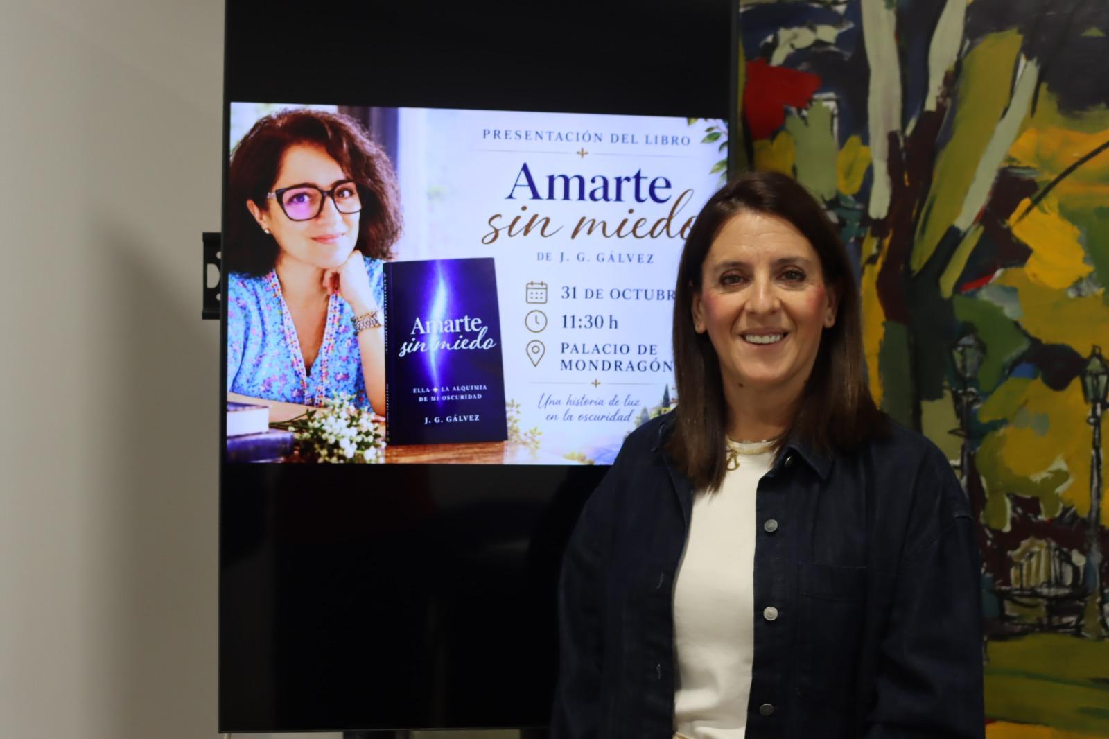 Una mujer sonriente posa junto a una pantalla que muestra el cartel de presentación del libro Amarte sin miedo.