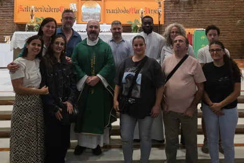 Un grupo de once personas posa sonriente en el interior de una iglesia, con un sacerdote de verde en el centro y un altar al fondo.