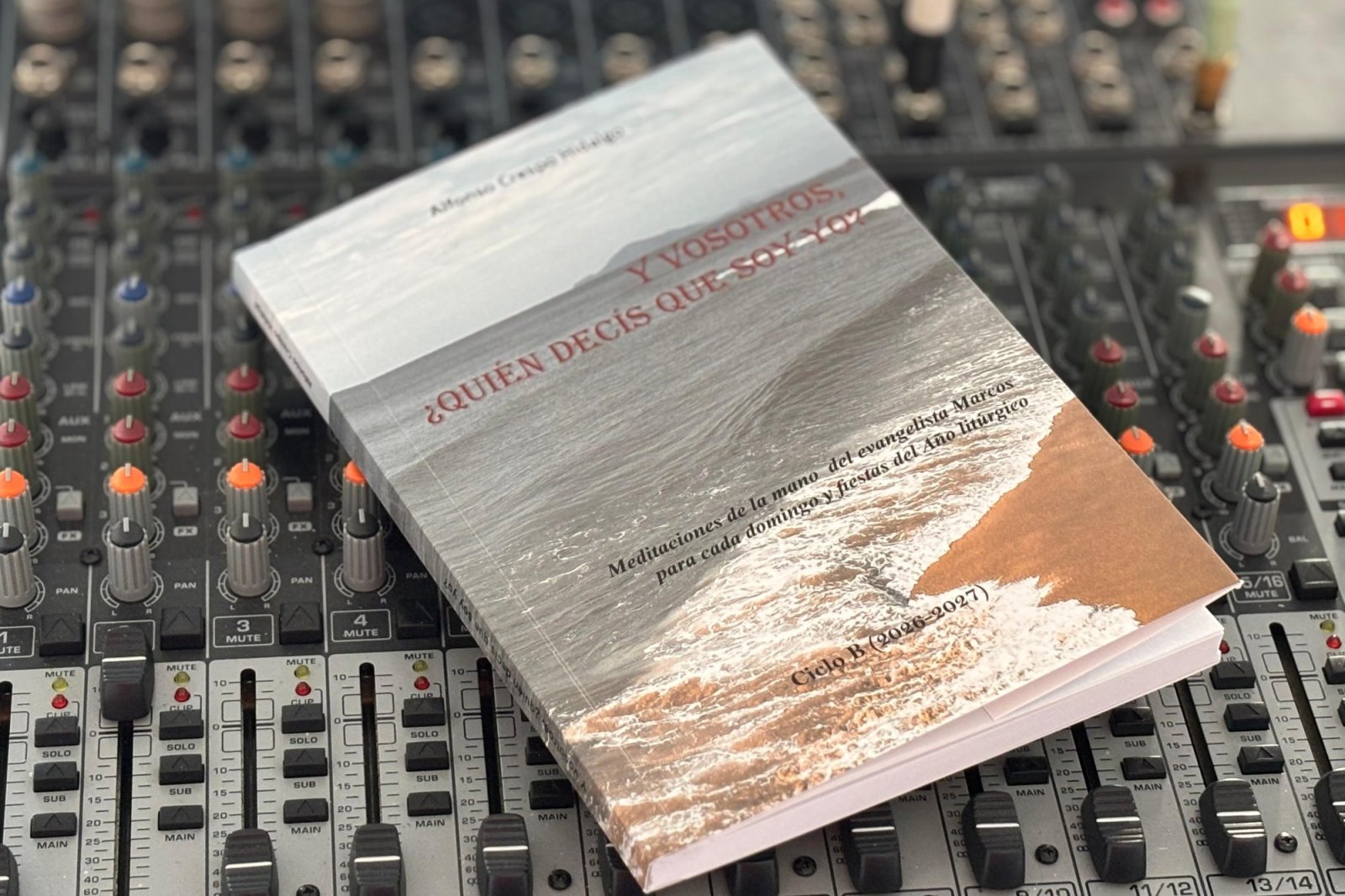 Un libro de tapa blanda con una playa en la portada descansa sobre una mesa de mezclas de audio.