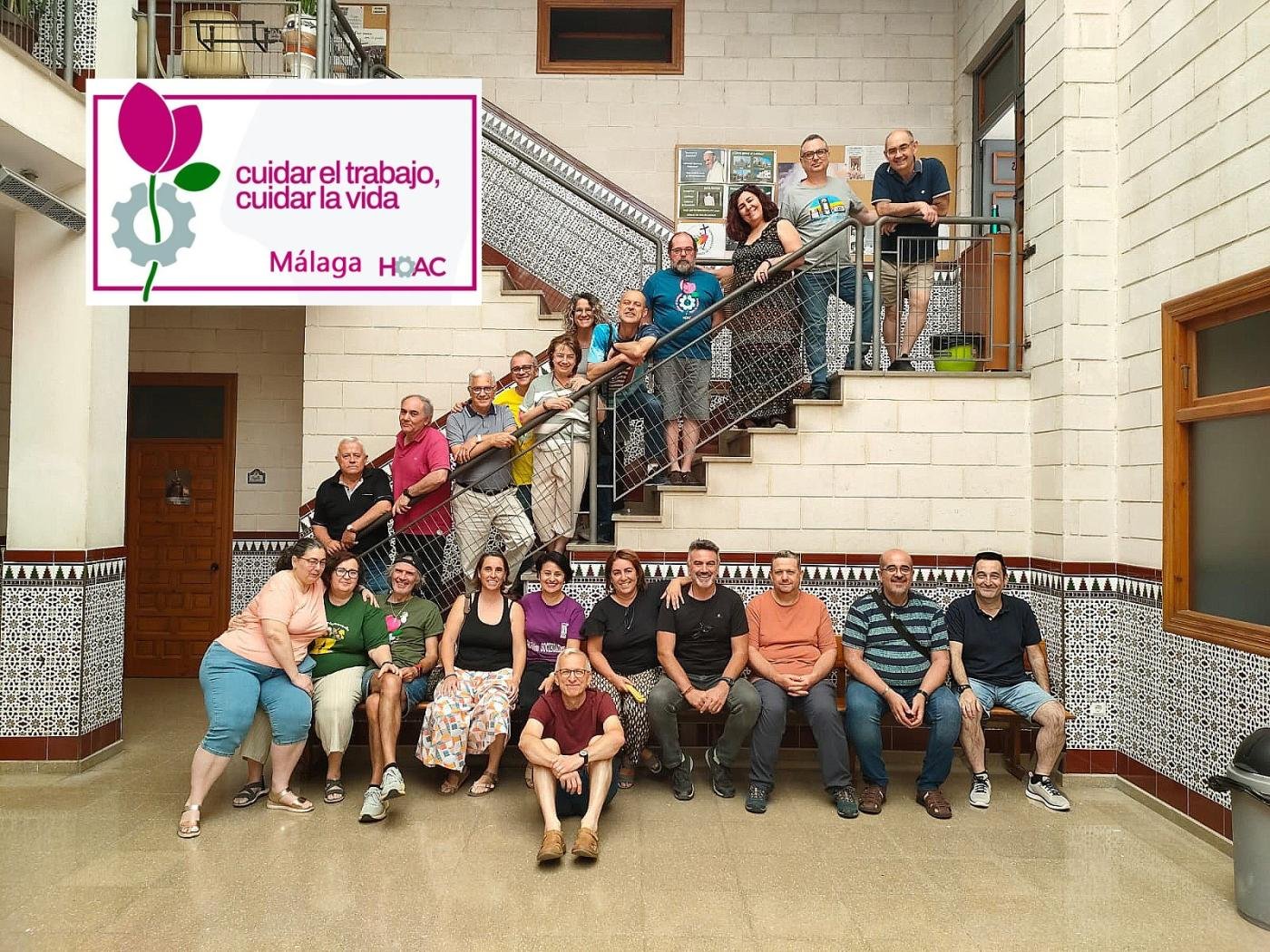 Un grupo de unas veinte personas posa sonriendo en una escalera y un banco de un patio interior con paredes de ladrillo y azulejos.