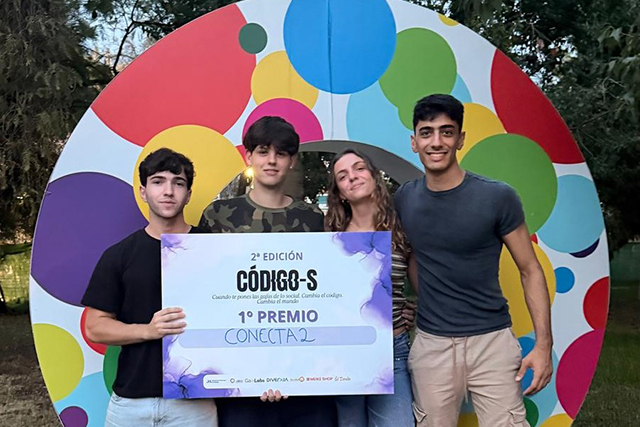 Cuatro jóvenes posan con un cartel de primer premio CÓDIGO-S ante un fondo circular de colores.