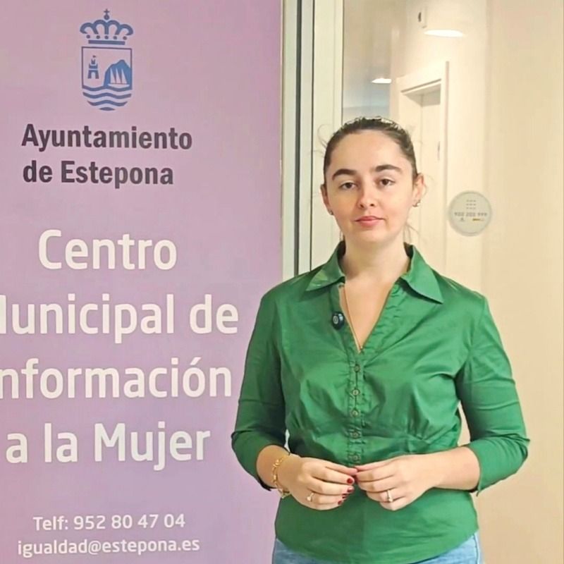 Una mujer con camisa verde de pie junto a un panel morado con el escudo y el texto Ayuntamiento de Estepona, Centro Municipal de Información a la Mujer.