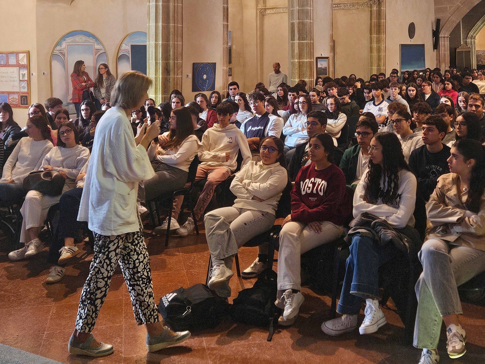 Una mujer de pie habla con micrófono ante un auditorio lleno de jóvenes sentados que la escuchan.